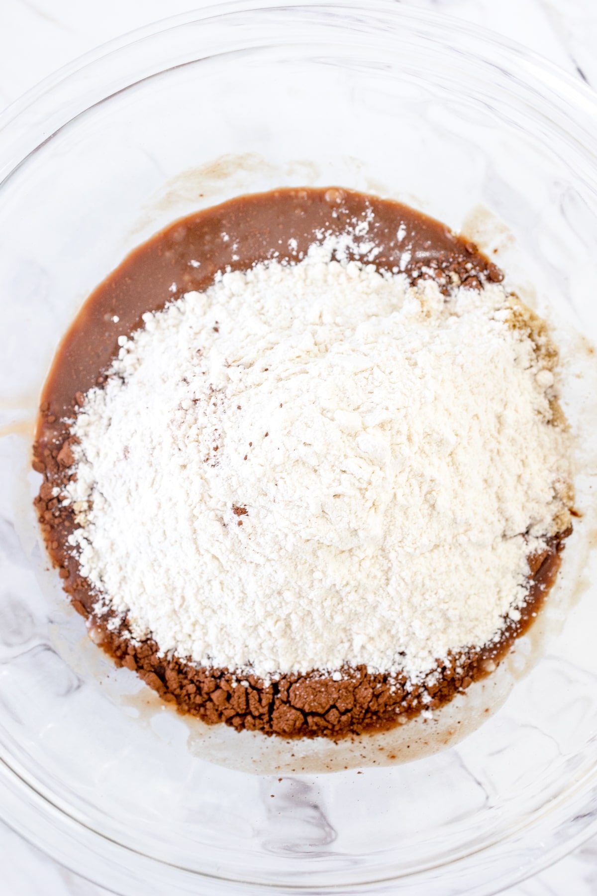 Top view of a glass mixing bowl with chocolate mixture in the bottom and white dry ingredients on top.