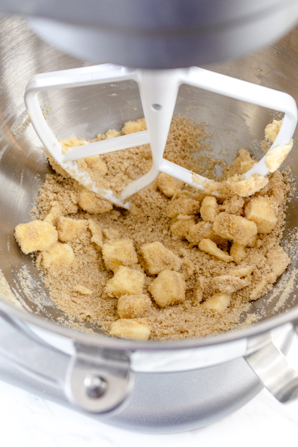Close up of the bowl of a stand mixer with a paddle attachment with cubed butter and sugars in it.