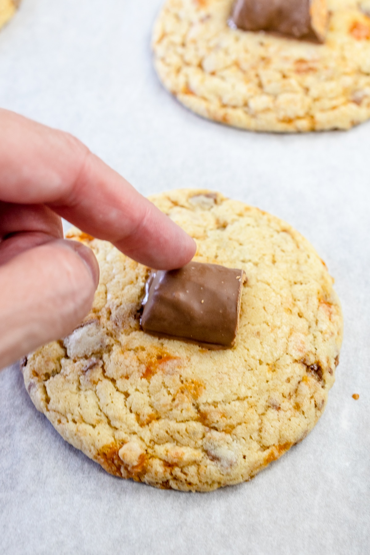 Close up of a freshly baked butterfinger cookie with someone putting a butterfinger candy on top.