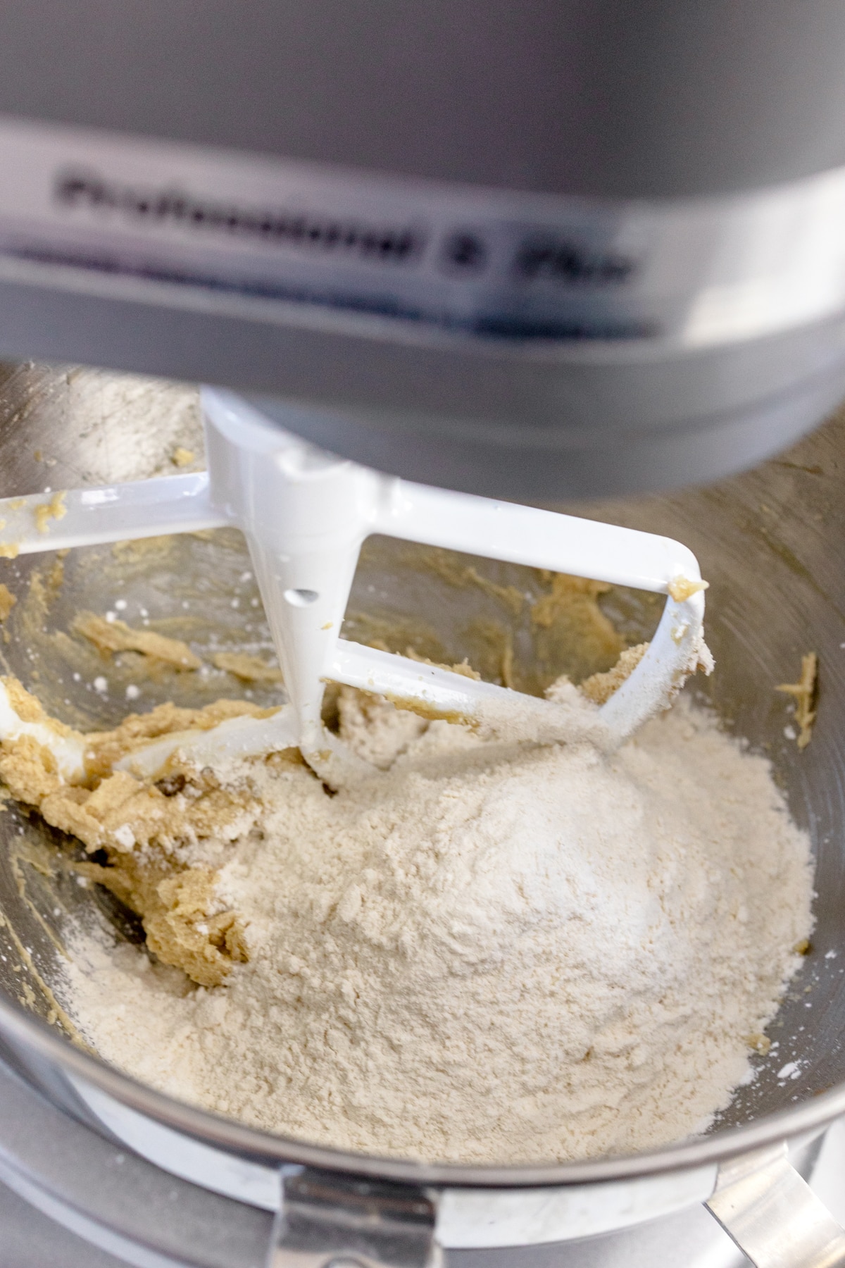 Close up of the bowl of a stand mixer with a paddle attachment mising creamed butter and sugars with a flour mixture.