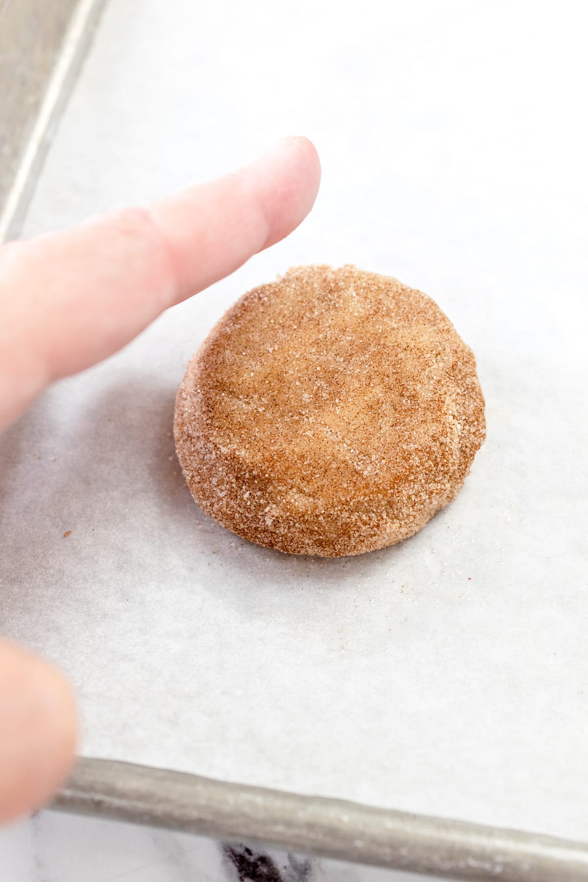 Cinnamon Churro Cookie dough ball about to be flattened with someone's finger.