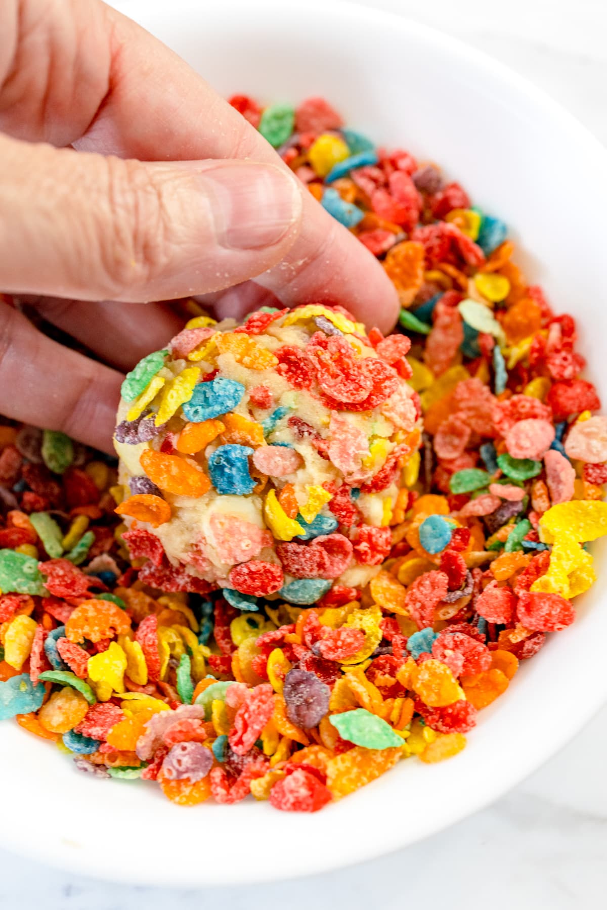Close up of a bowl of fruity pebbles cereal with a cookie being coated in the cereal in the bowl.