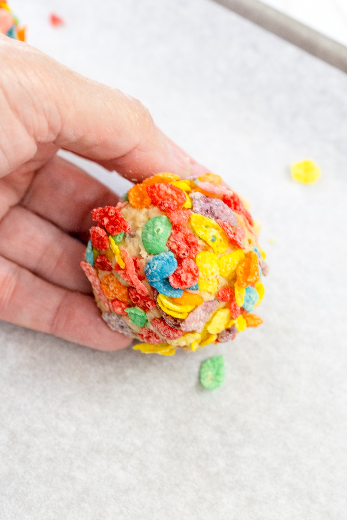 Top view of someone holding a ball of fruity pebble cookie dough in their hand.