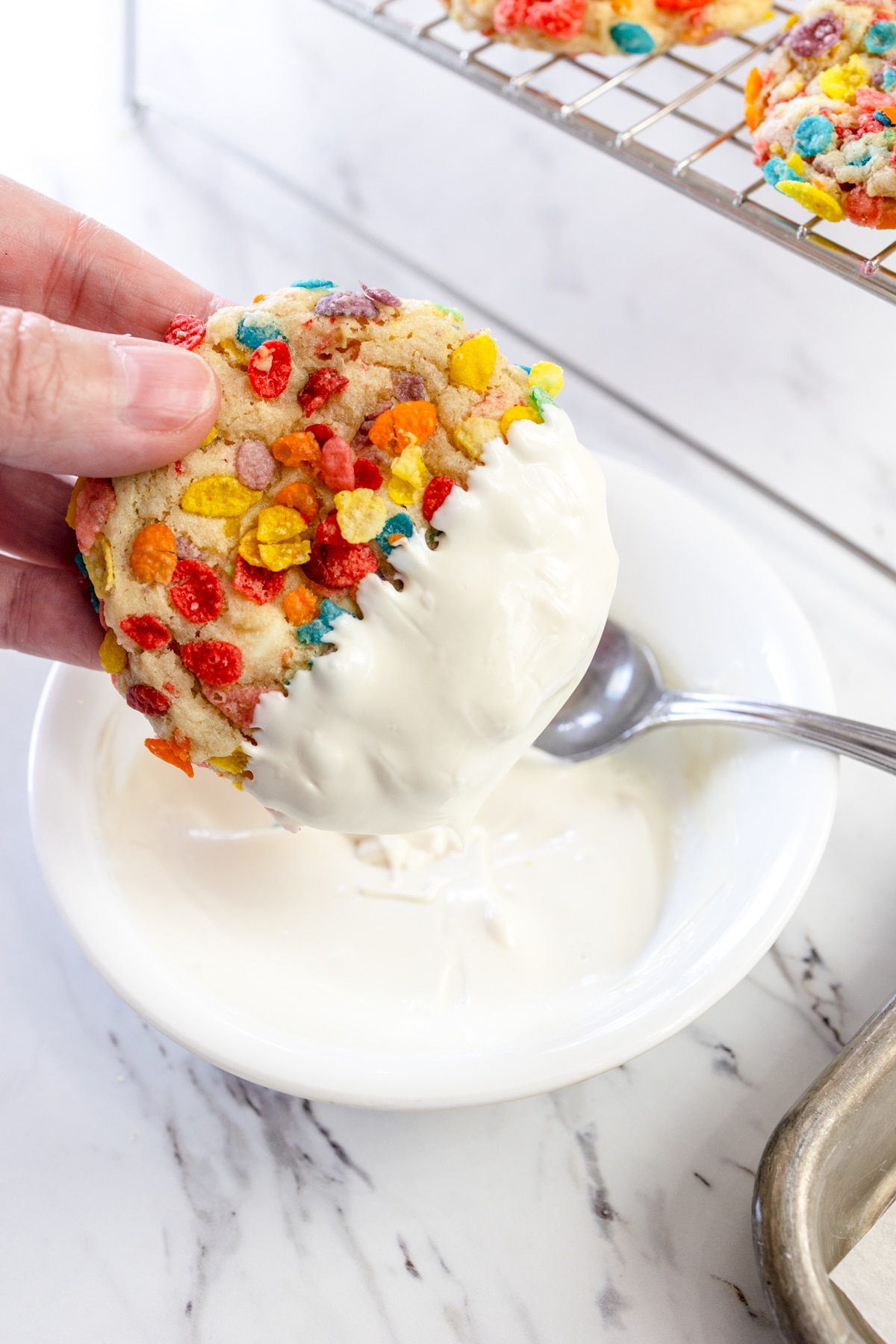 Top view of a Fruity Pebbles Cookie being dipped into melted white chocolate.