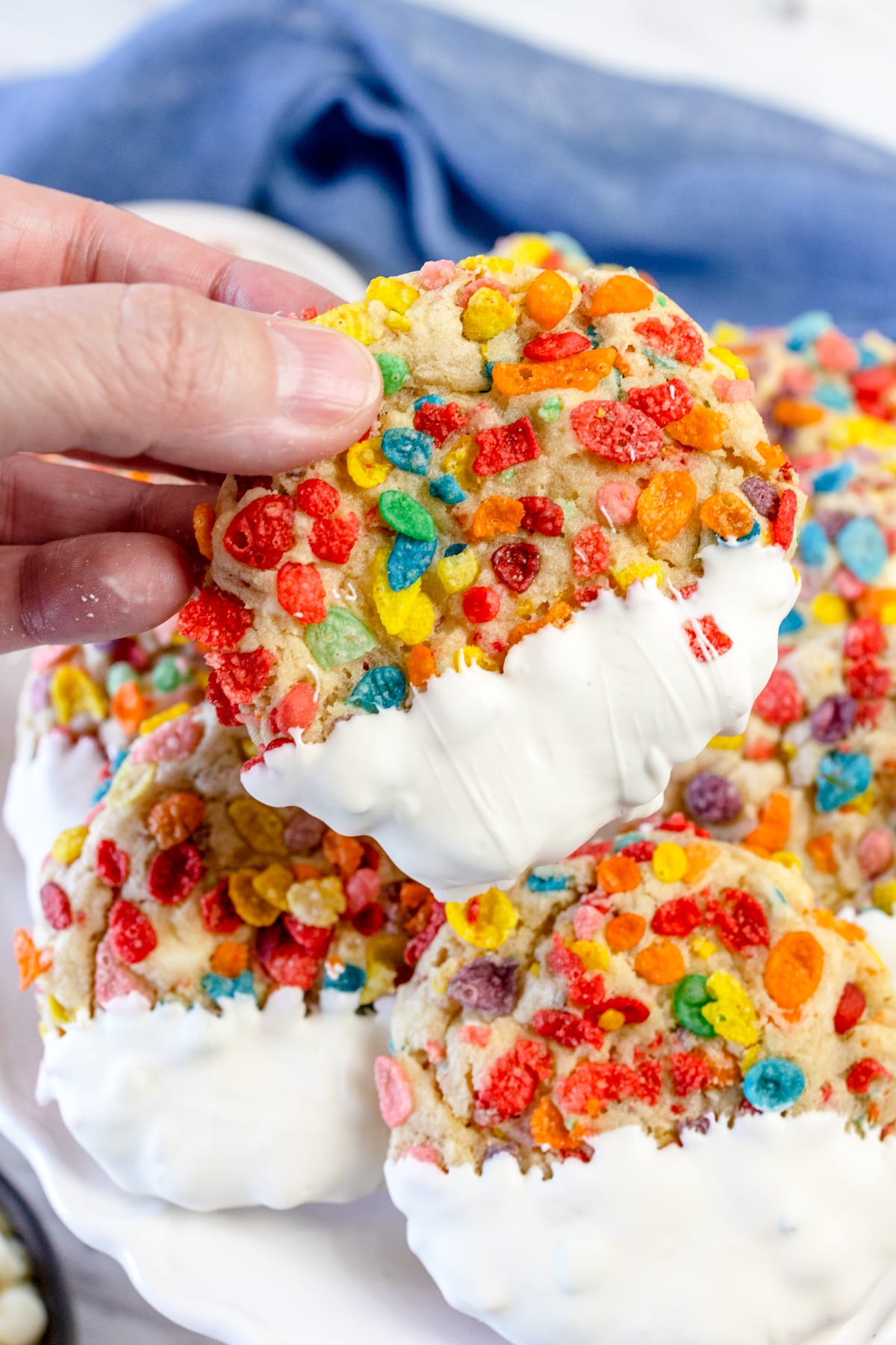 Close up of someone picking up a Fruity Pebbles Cookie off the top of a pile of cookies on a plate. 