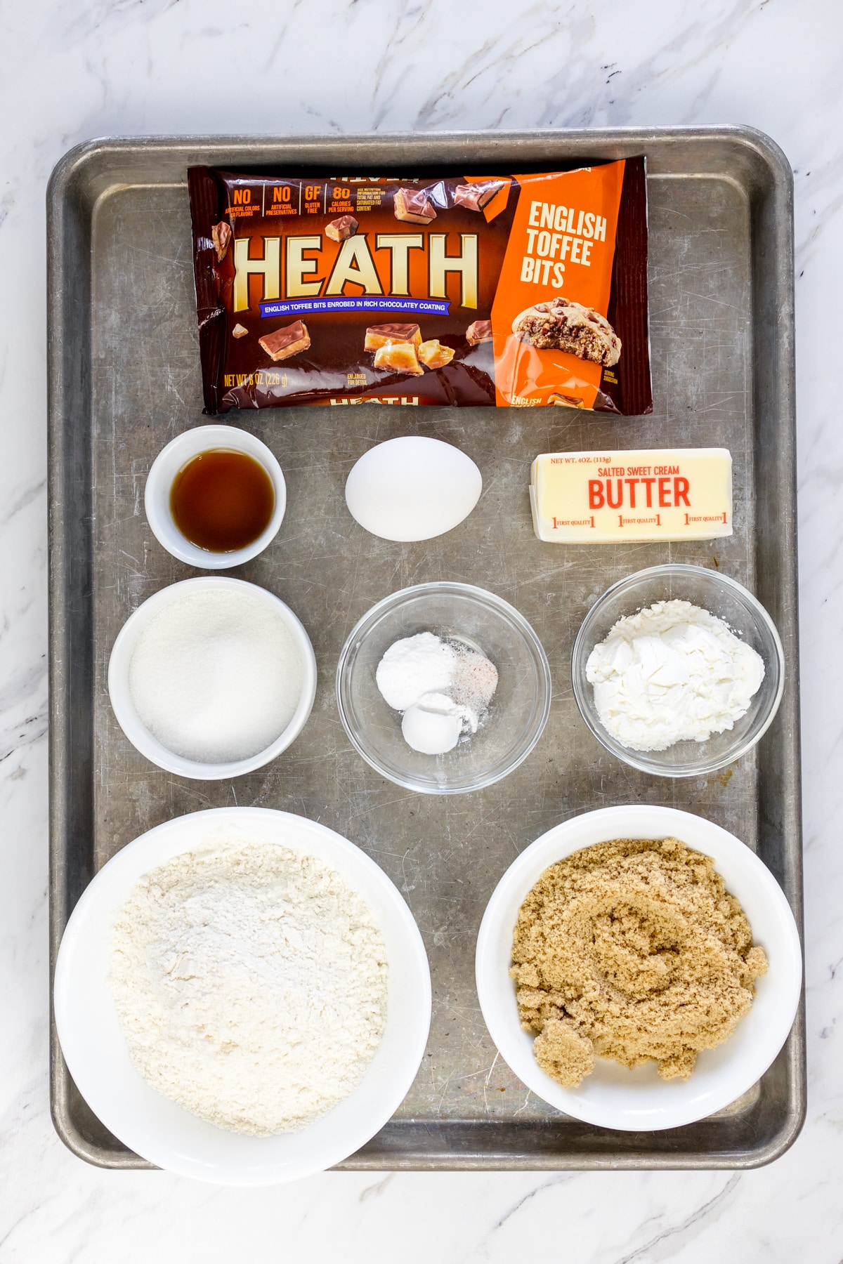 Top view of ingredients needed to make Heath Cookie Bars in small bowls on a baking tray.