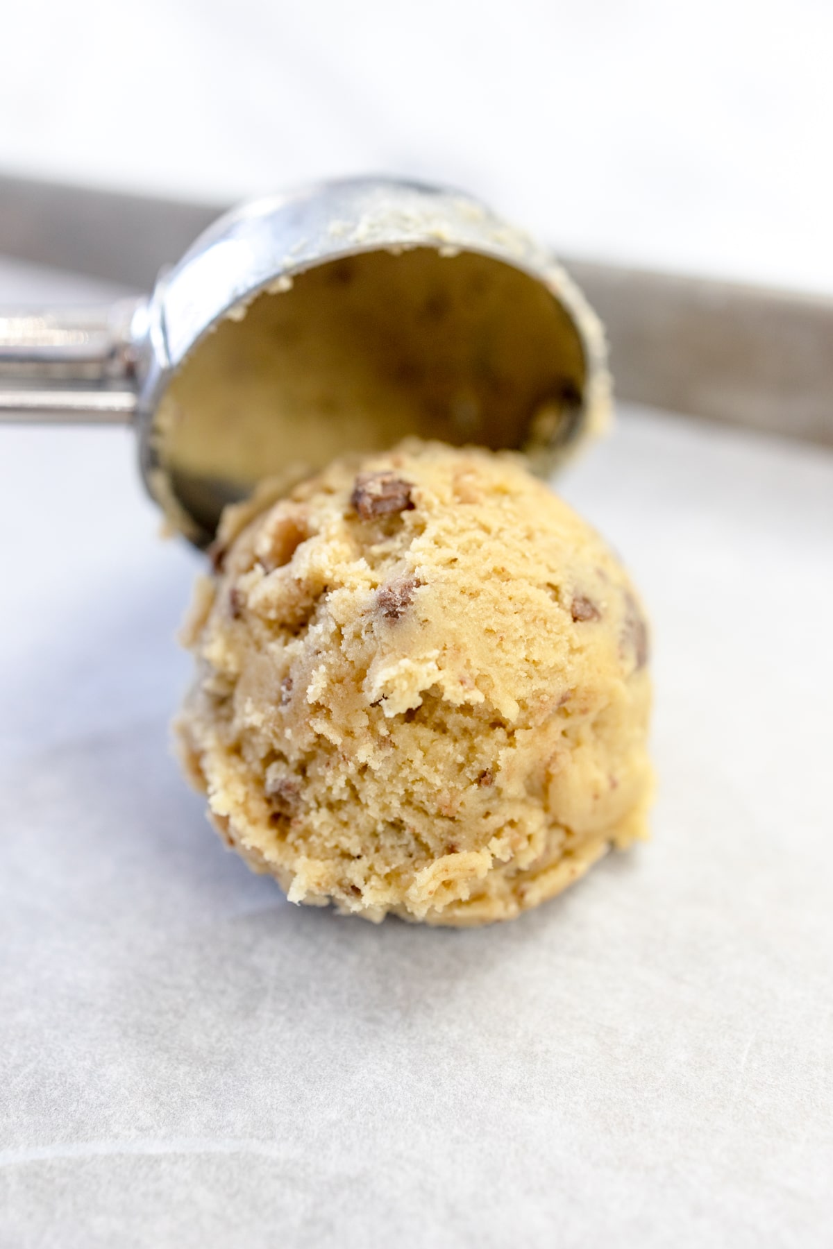 Close up of a cookie dough ball being placed onto a parchement lined baking tray with a cookie scoop.