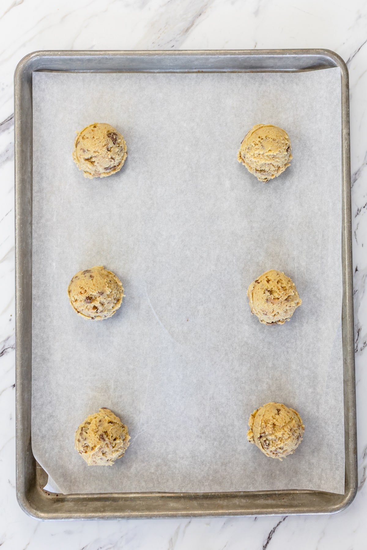 Top view of cookie dough balls on parchment paper on a baking tray.
