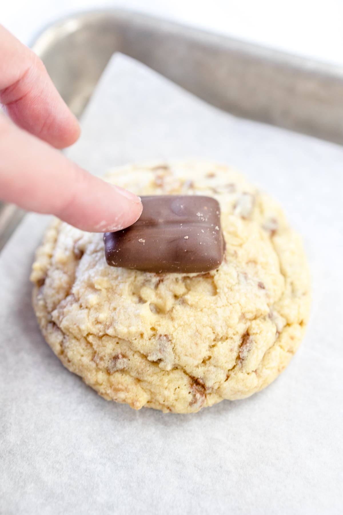 Close up of a cookie being topped with a Heath Bar.