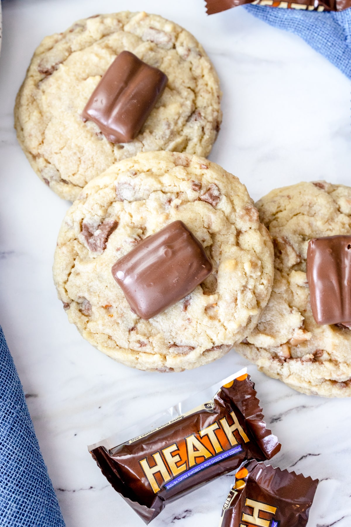 Top view of Heath Bar Cookies on a plate with heath bar candies in wrappers next to them.