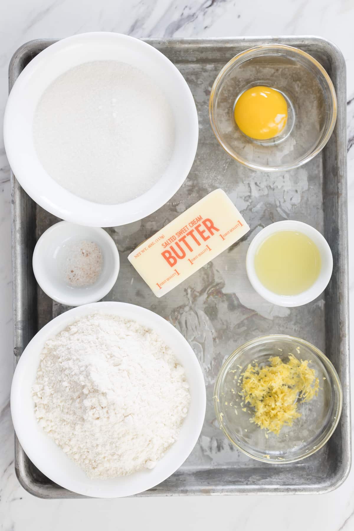 Top view of ingredients needed to make lemon shortbread cookies in small bowls on a tray.