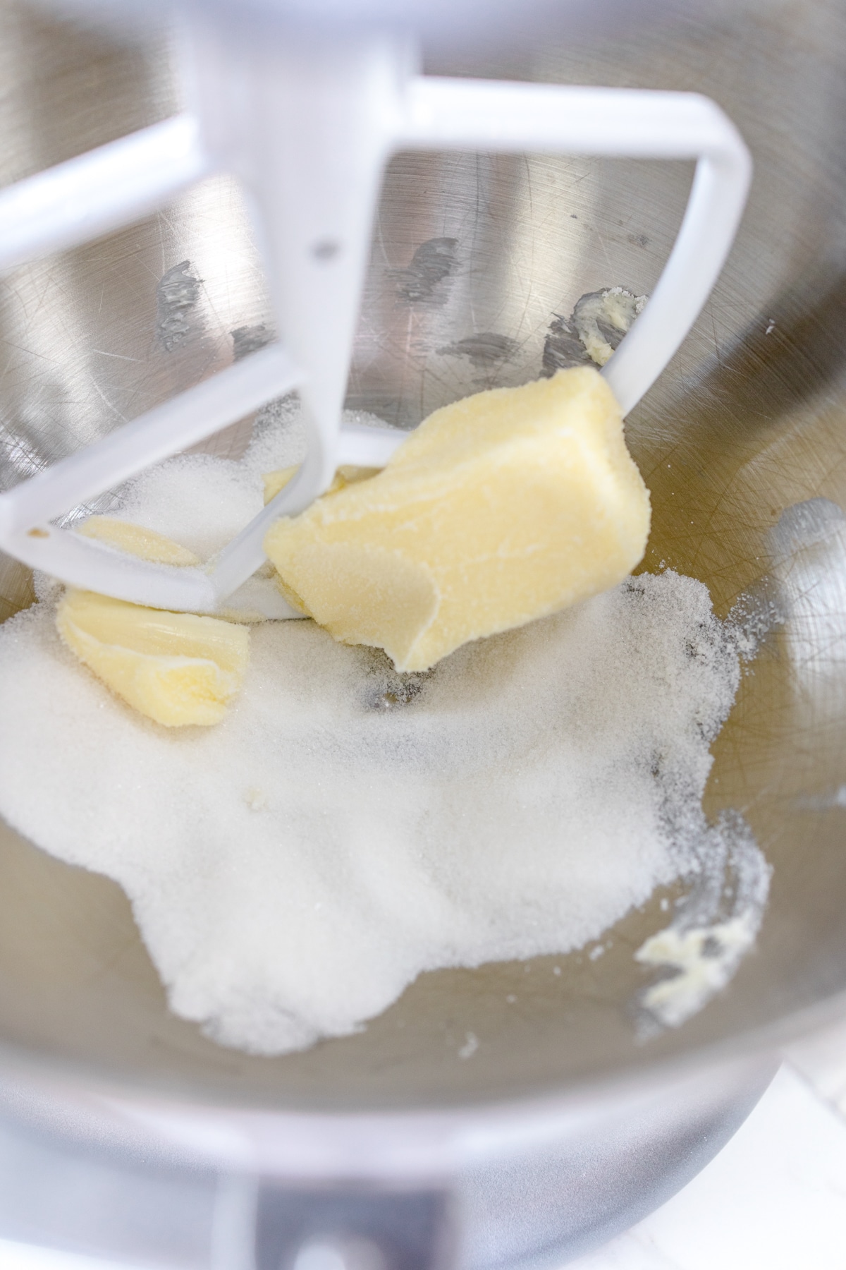 Close up of the bowl of a stand mixer with cold butter cubes and wite sugar beig mixed with a paddle attachment.