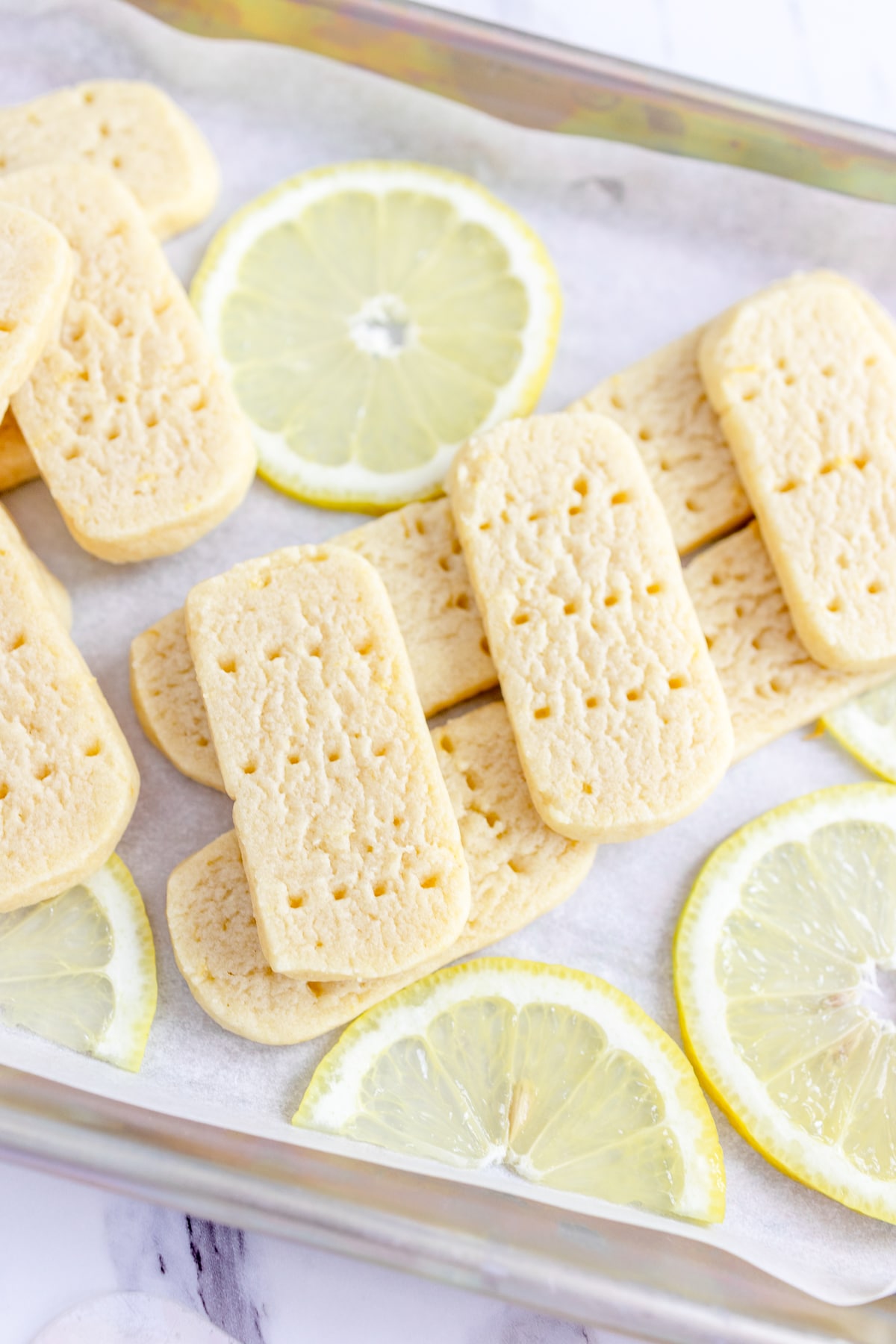 Top view of Shortbread Cookies on a baking tray surrounded by slices of fresh lemon.