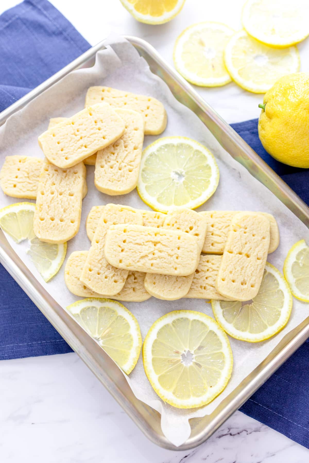 Top view of Lemon Shortbread Cookies on a baking tray surrounded by slices of fresh lemon.