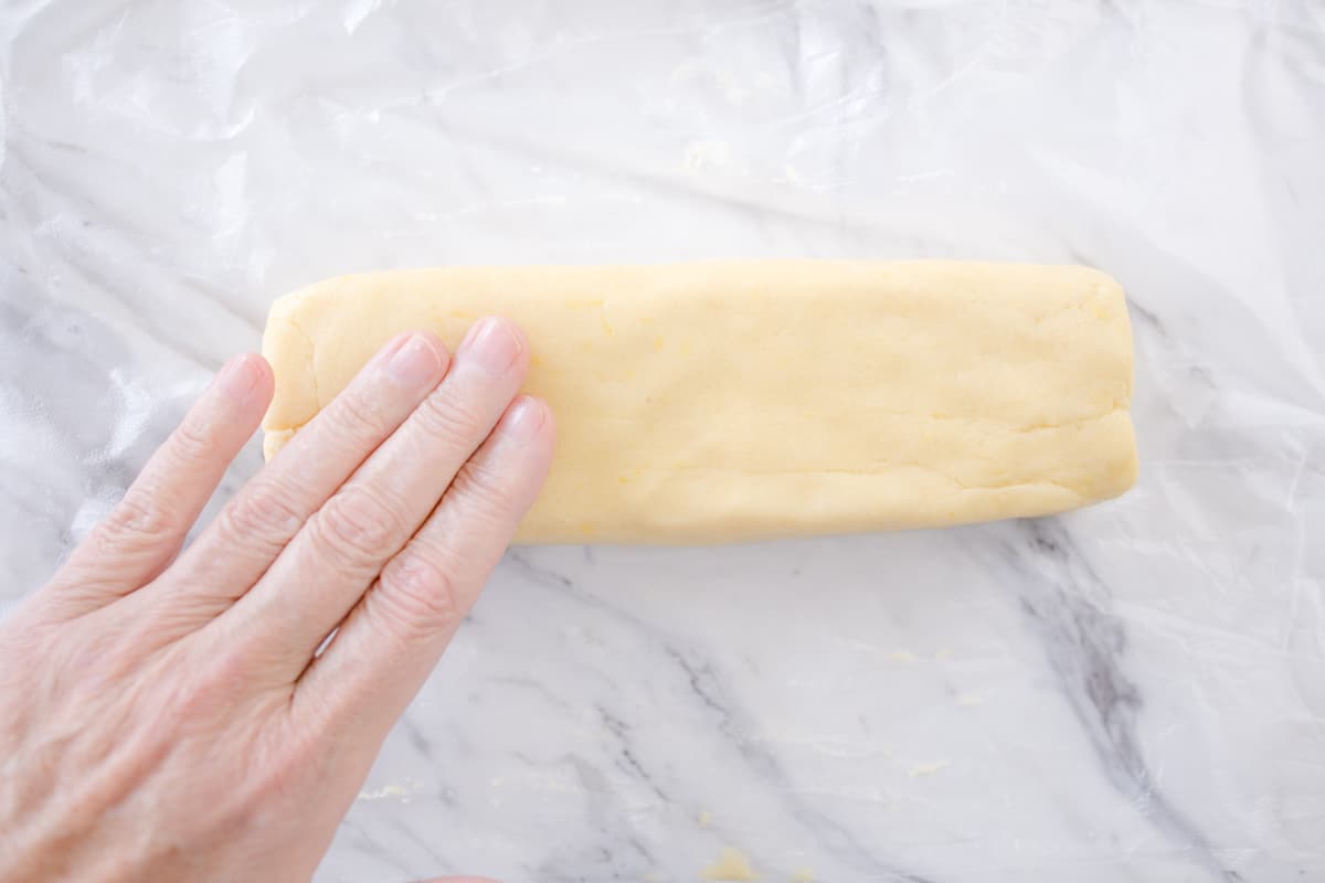 Top view of lemon shortbread cookie dough in a rectangle shape with a hand on it.
