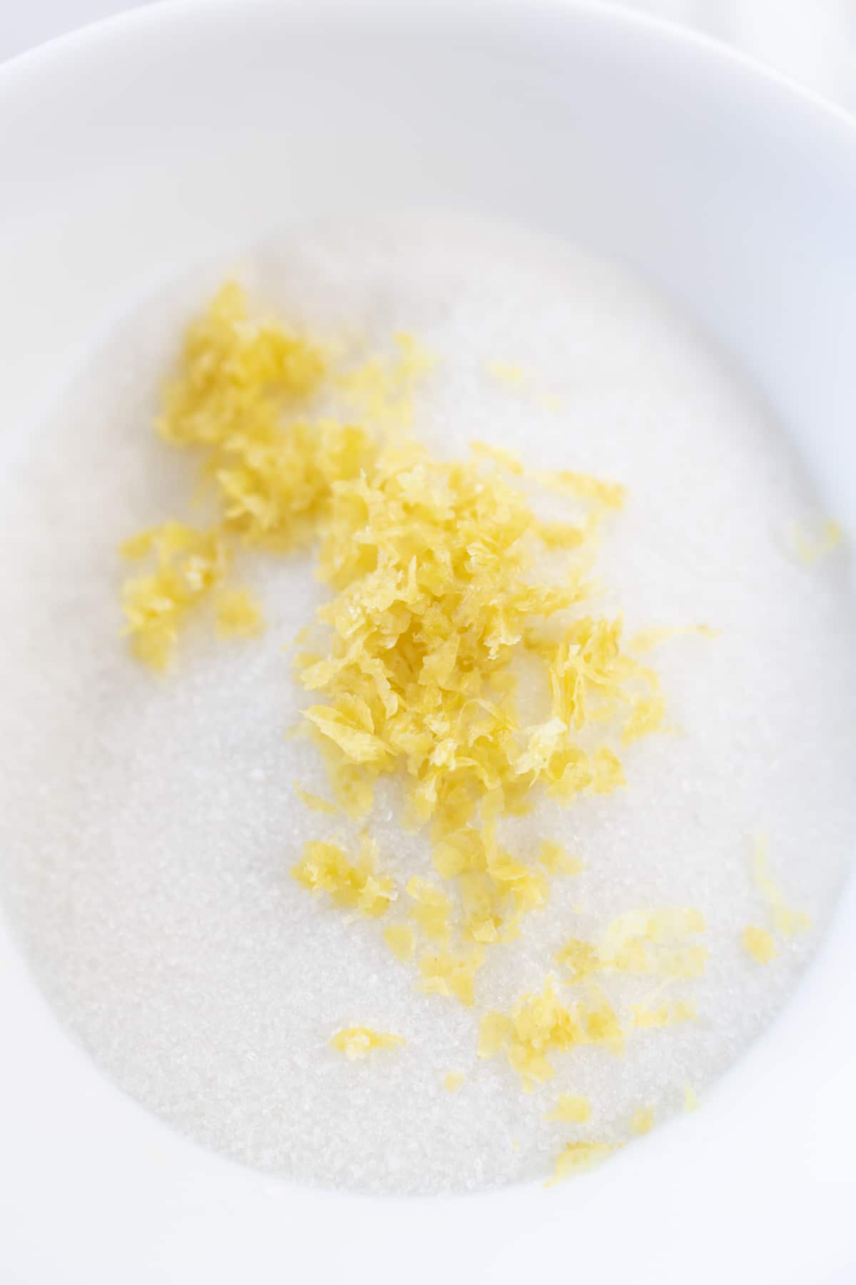 Top view of lemon zest and white sugar in a white bowl.