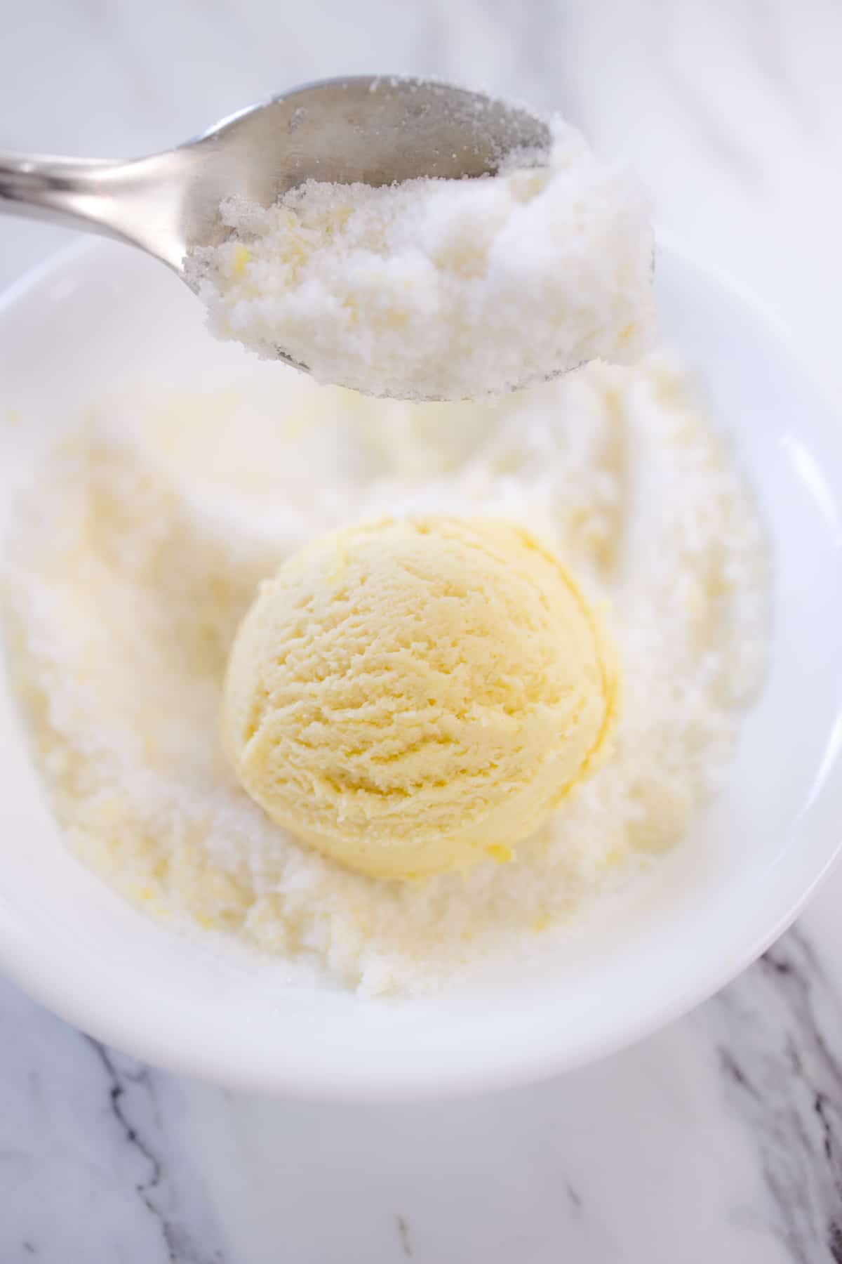 Close up of a lemon cookie dough ball being rolled in a bowl of lemon zest and sugar. t