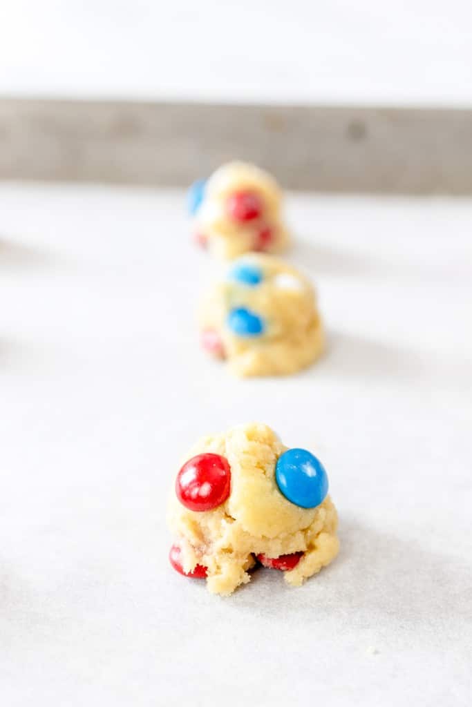 Close up of Mini Mini M&M cookie dough balls on parchment paper on a baking tray.