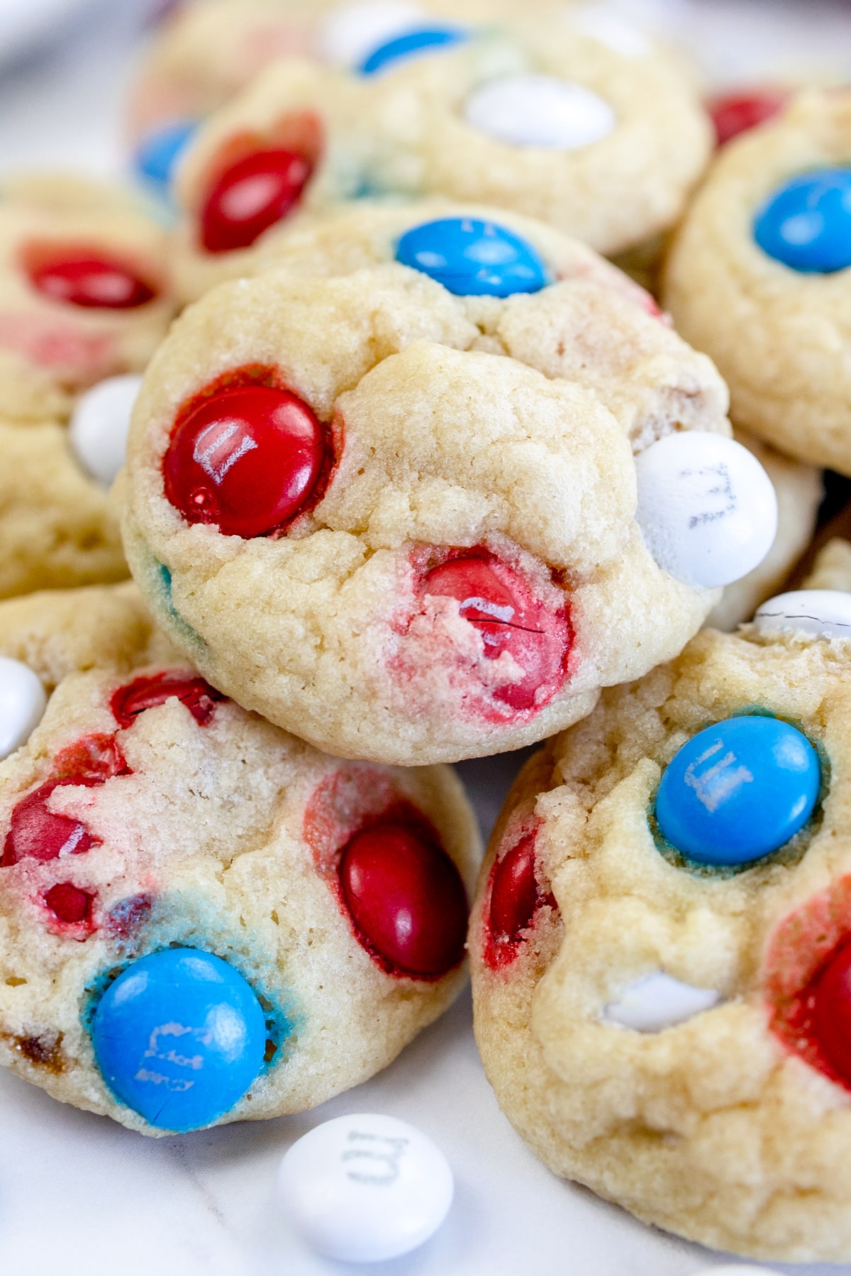 Close up of Mini M&M cookies in a pile on a white surface. 