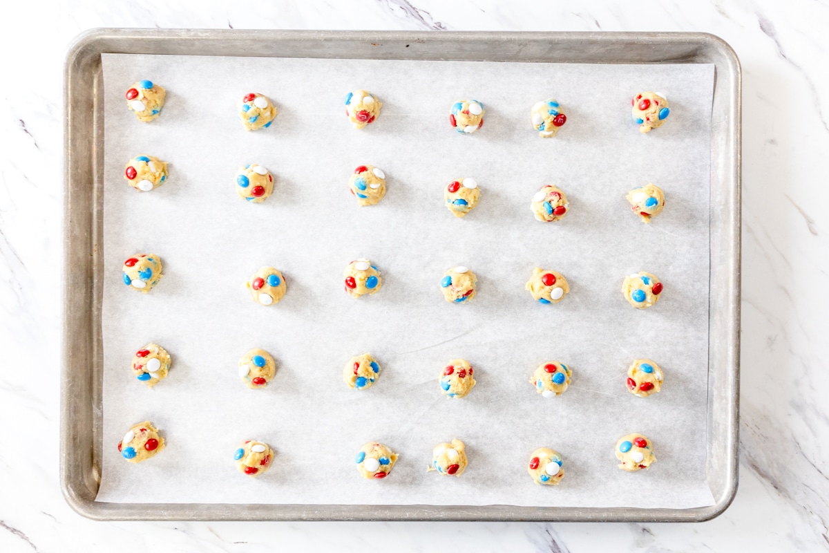 Top view of mini Mini M&M cookie dough balls in a grid pattern on patchment paper on a baking tray.
