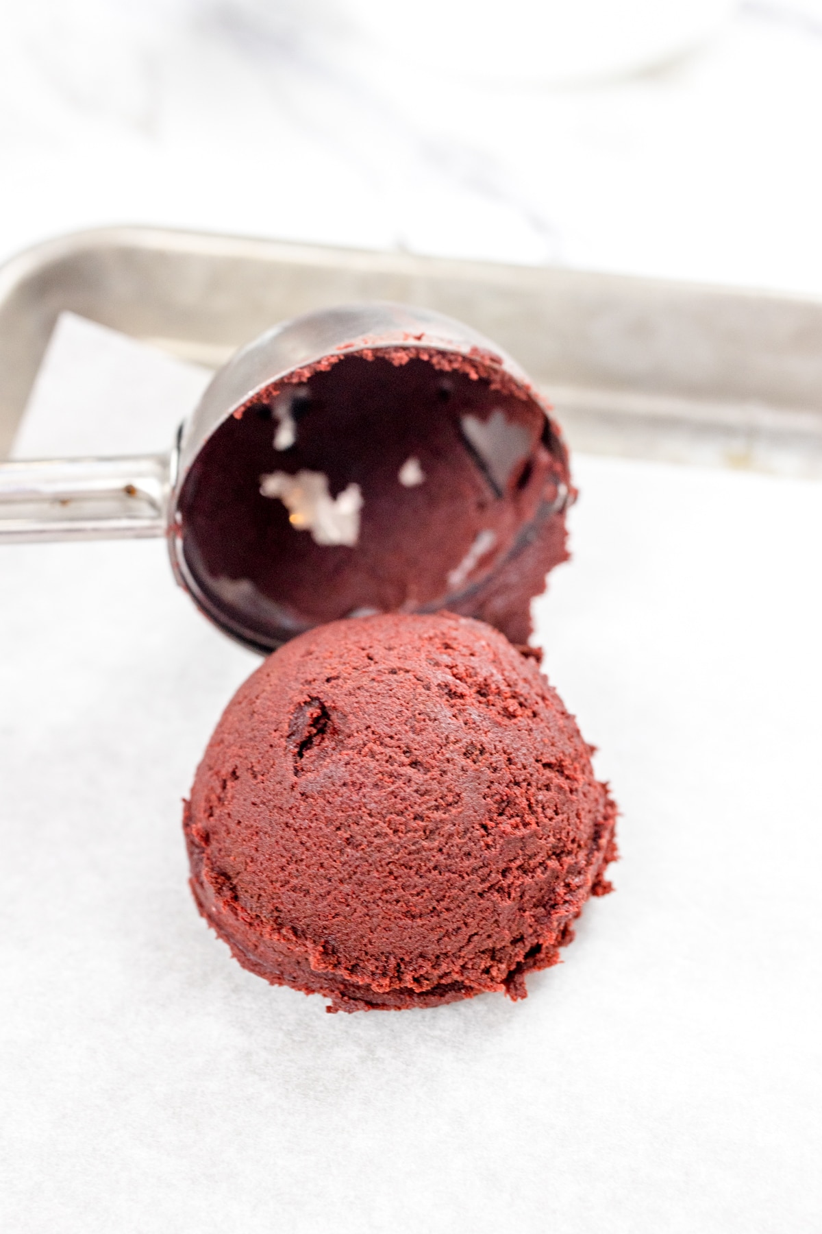 close up of a cookie scoop placing a red velvet cookie dough ball on parchment paper.