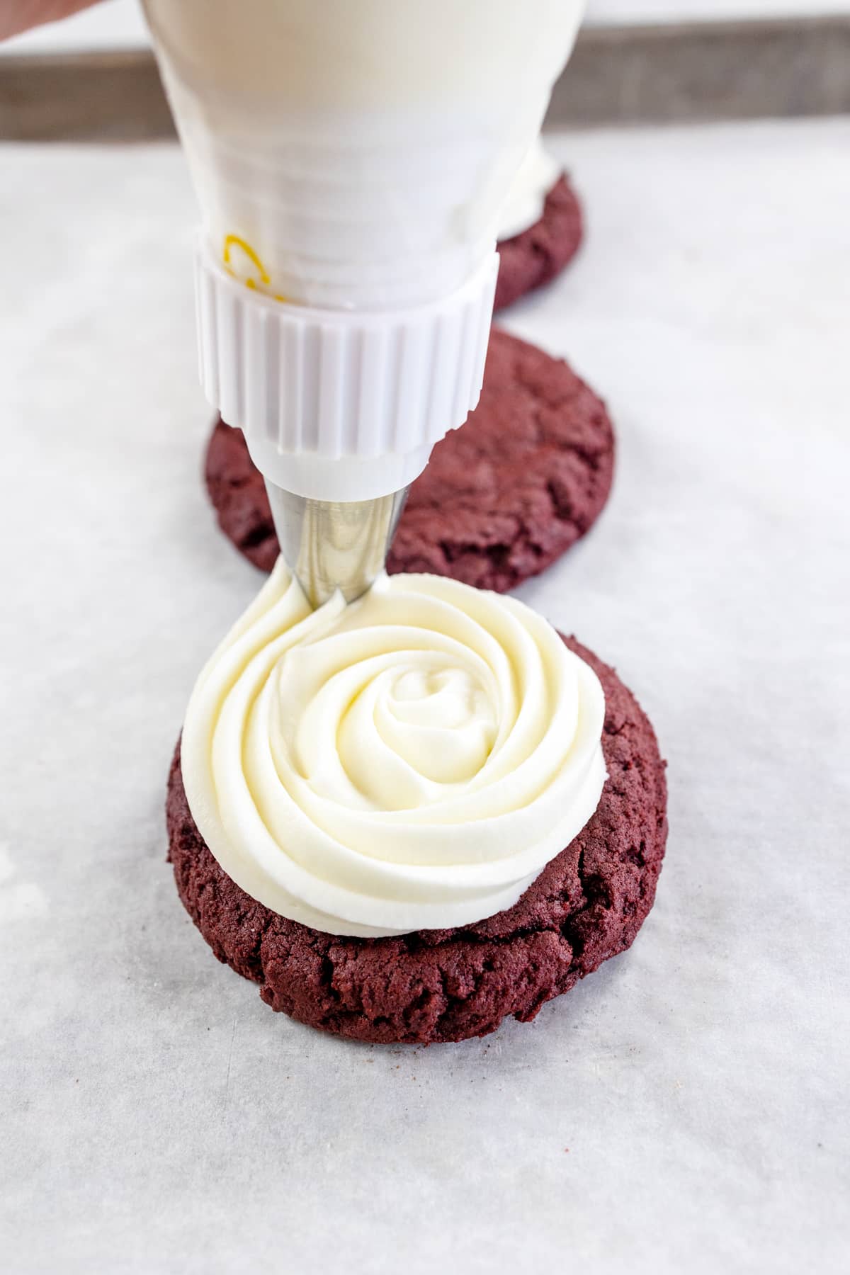 Close up of a Red Velvet Cookie being topped with Cream Cheese Frosting.