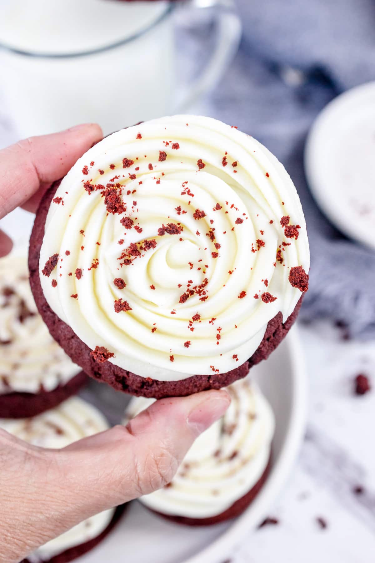 Top view of a Red Velvet Cookies with Cream Cheese Frosting being held in mid air by a hand.