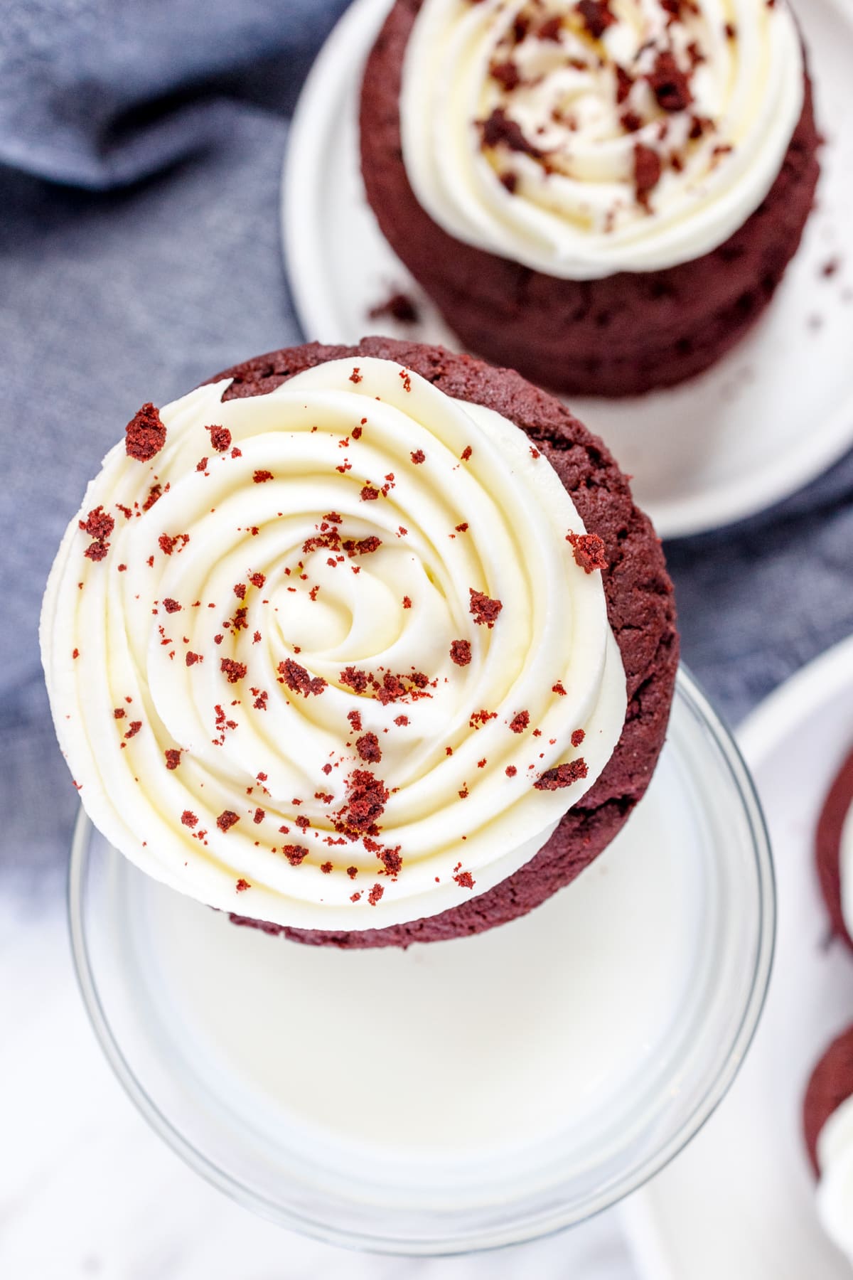 Top view of a Red Velvet Cookie with Cream Cheese Frosting balancing on the rim of a glass filled with milk.