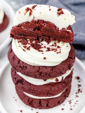 A stack of Red Velvet Cookies with Cream Cheese Frosting on a white plate.