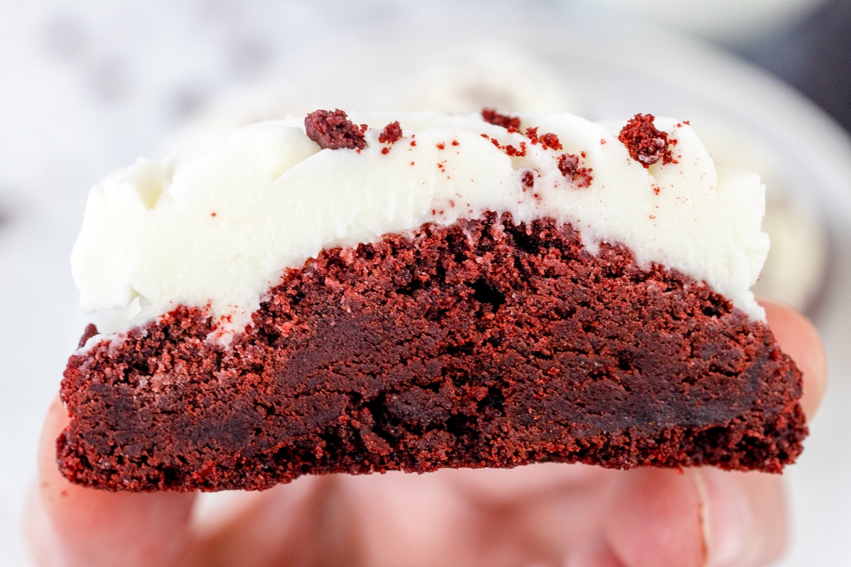 Close up of a Red Velvet Cookie cut in half, being held in mid-air so you can see the chewy inside.