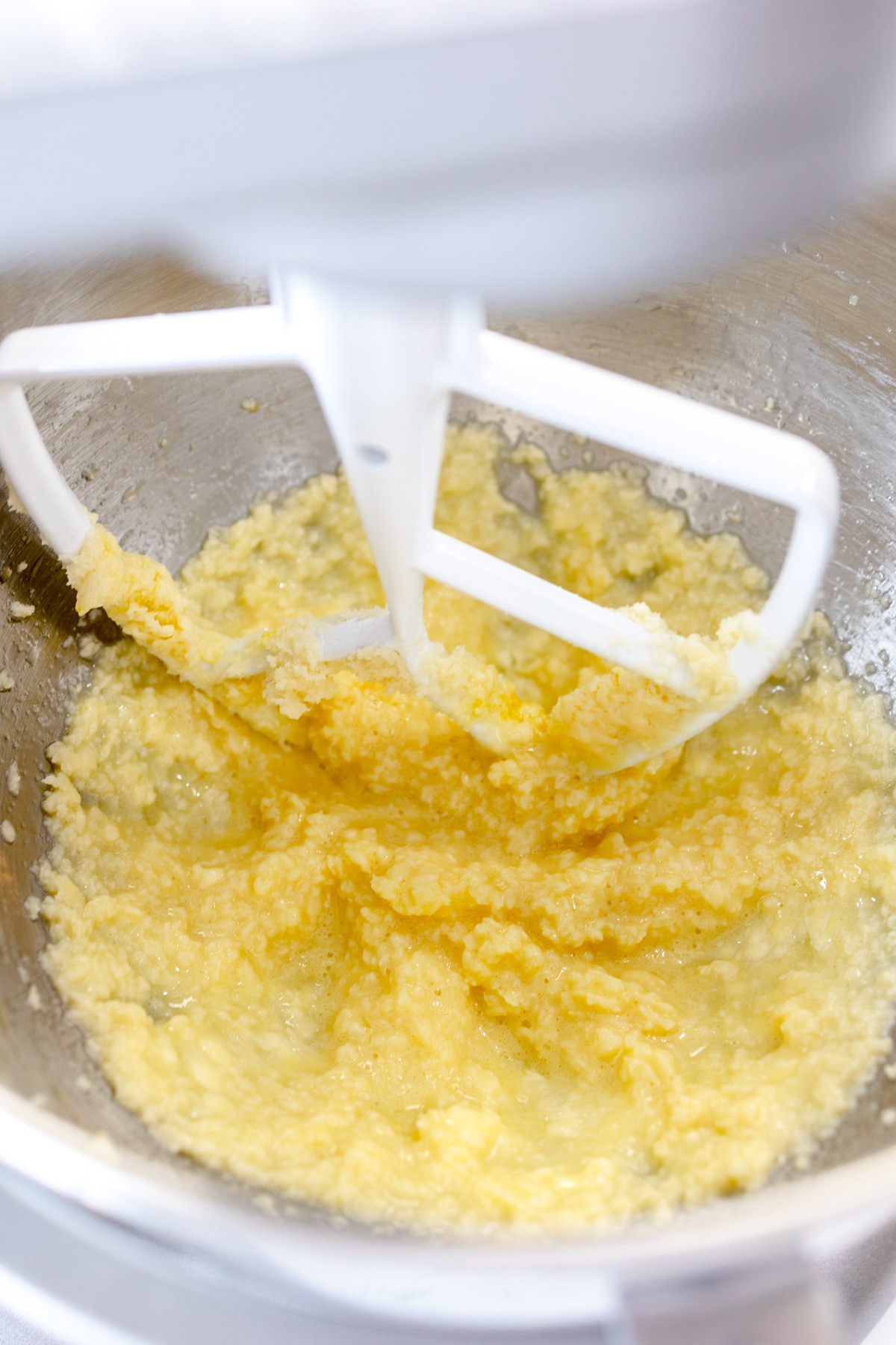 Close up of the bowl of a stand mixer with a paddle attachment creaming butter and sugar.