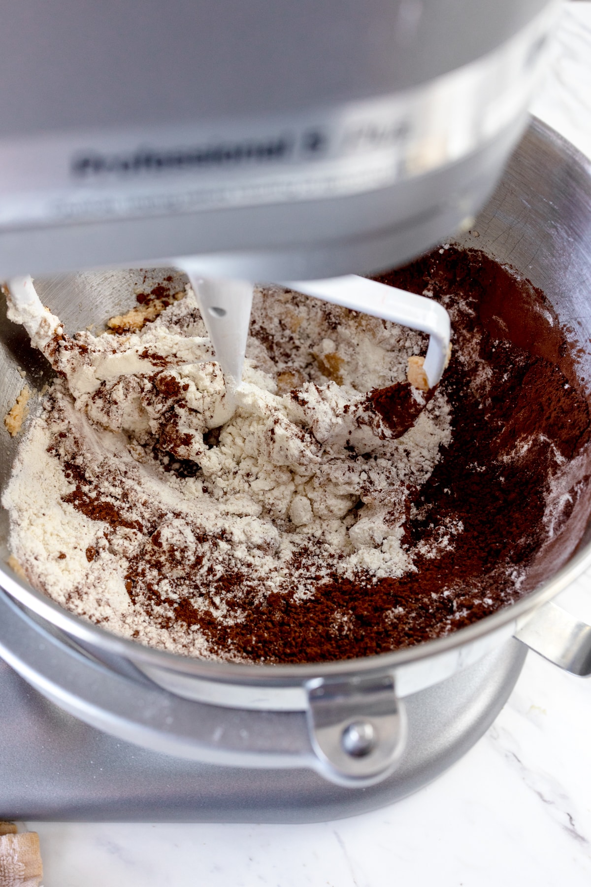 Close up of the bowl of a stand mixer with a creamed mixture in the bottom, and a cocoa powder and flour mixture on top.