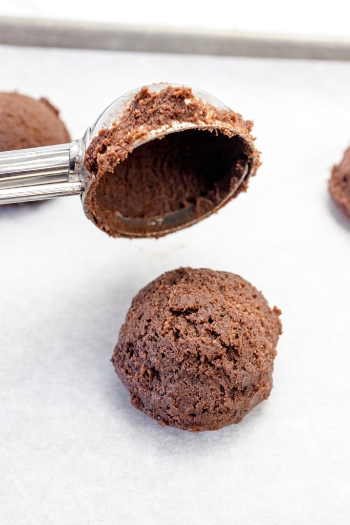 A cookie scoop putting a ball of chocolate cookie dough on a parchment lined baking tray.