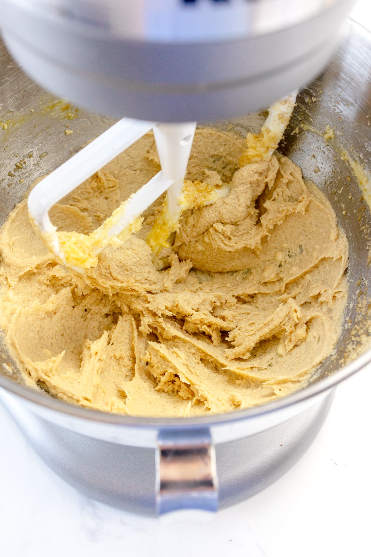 Close up of the bowl of a stand mixer, mixing cookit dough with a paddle attachment.