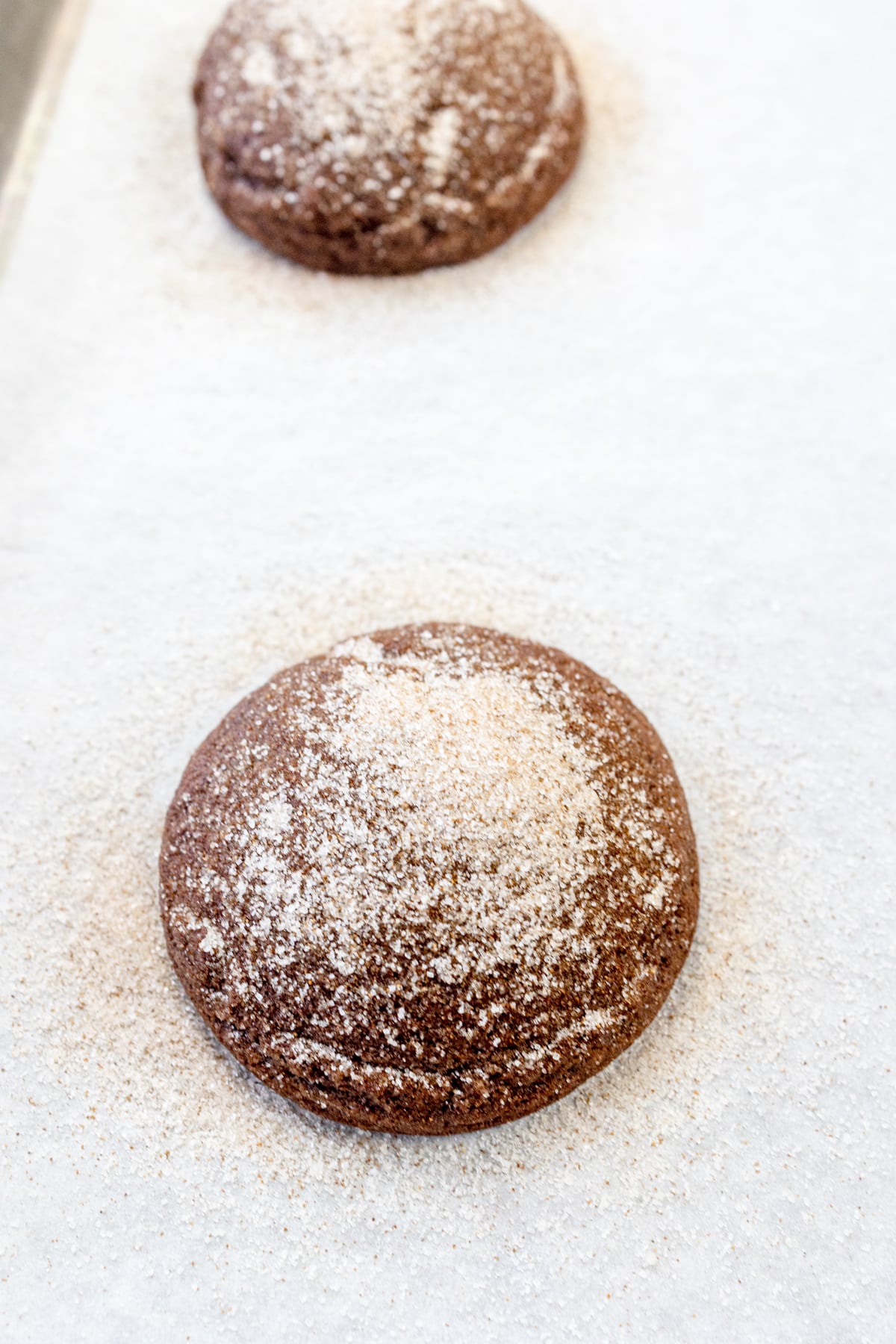 Close up of a chocolate cookie with cinnamon sugar on it on parchment paper on a baking tray.