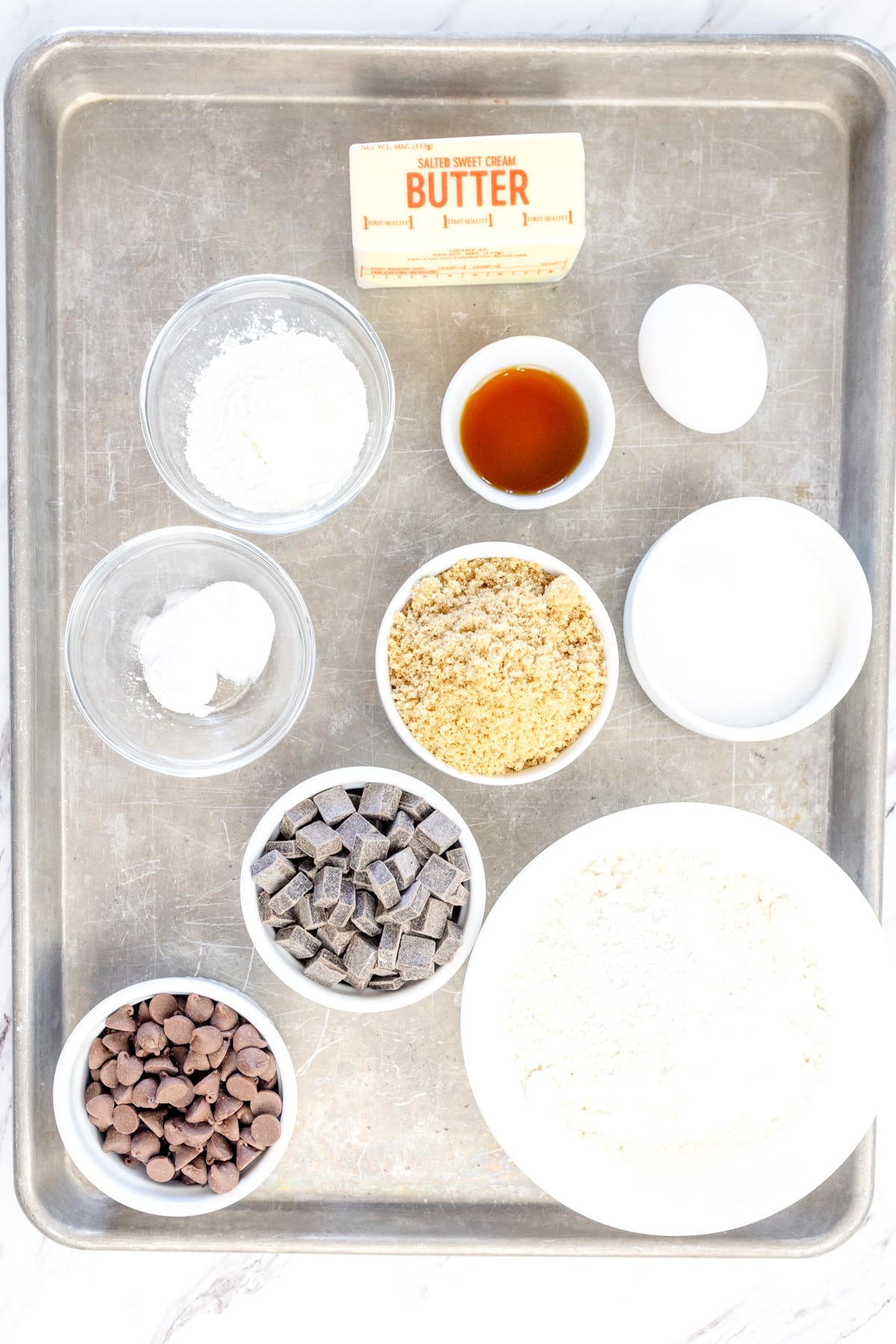 Top view of ingredients needed to make Frosted Chocolate Chip Cookies in small bowls on a baking tray. 