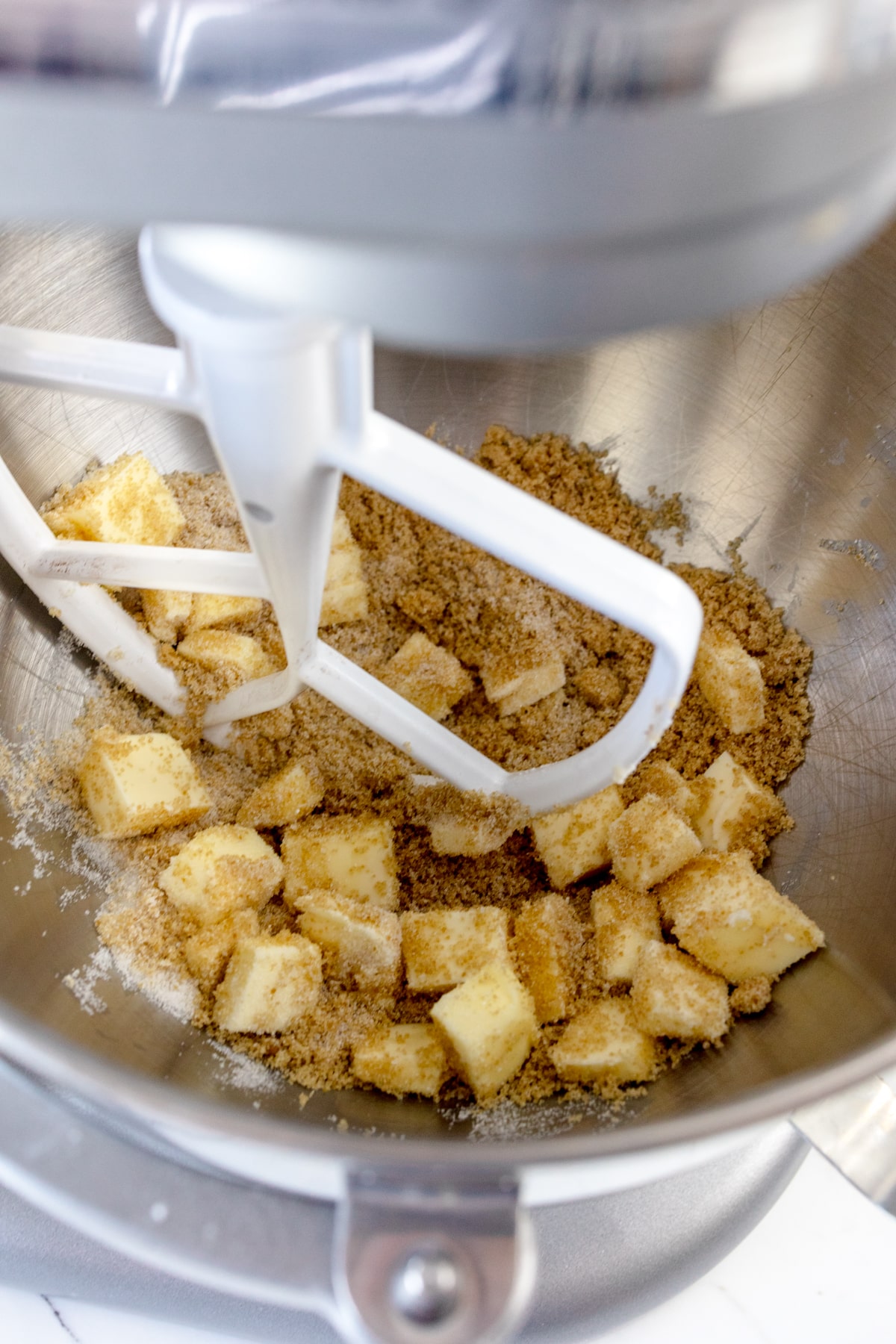 Close up of the bowl of a stand mixer with butter squares and brown sugar in it. 