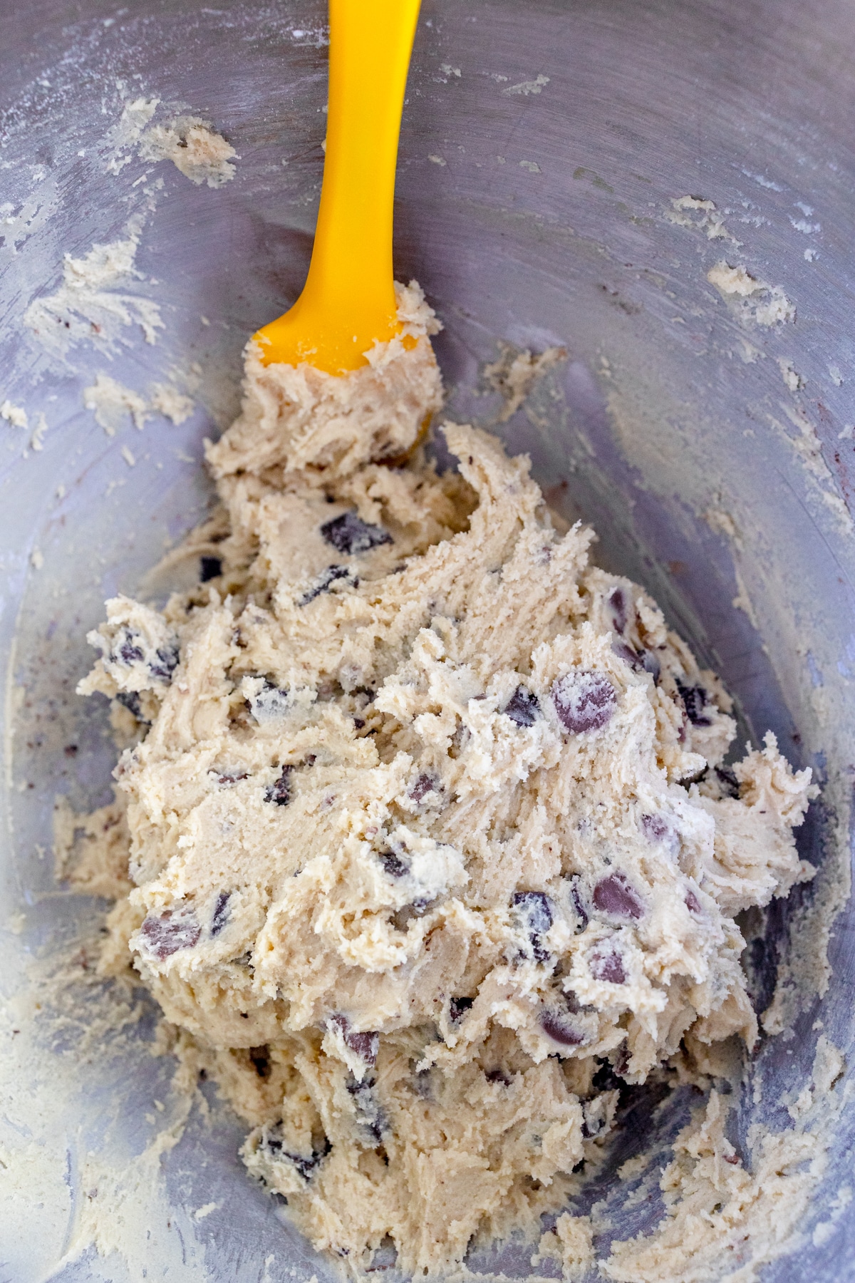 Close up of the bowl of a stand mixer with a ywllo spatula scraping the sied of the bowl with cookie dough in it.