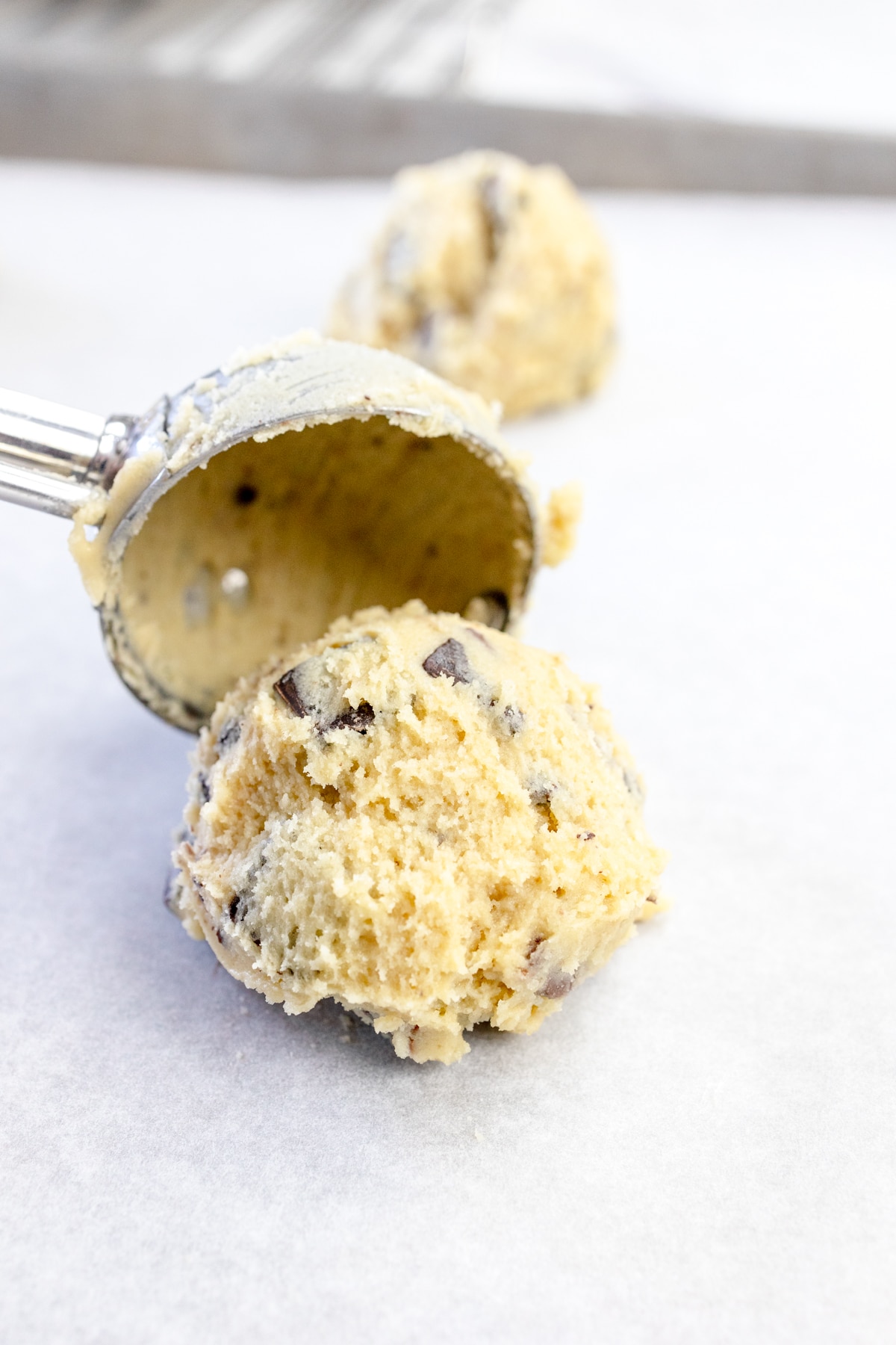 Close up of a cookie scoop putting a cookie dough ball onto parchemnt paper.