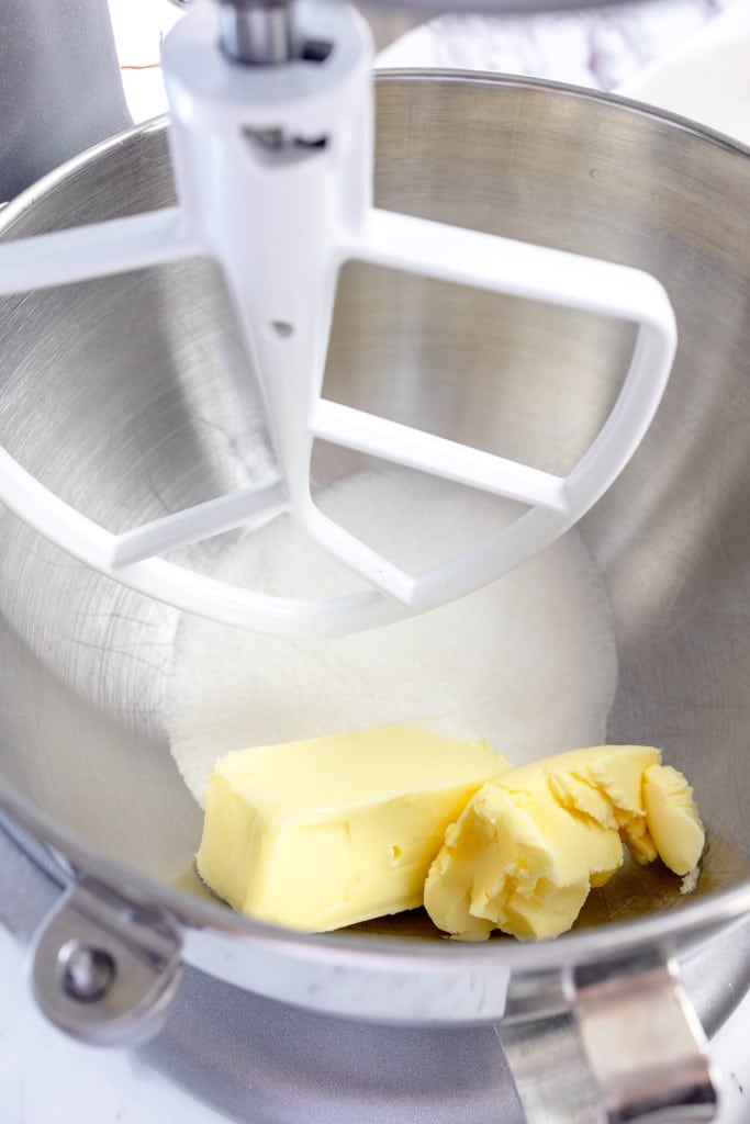 Close up of the bowl of a stand mixer with butter and sugars in it with a paddle attachment.