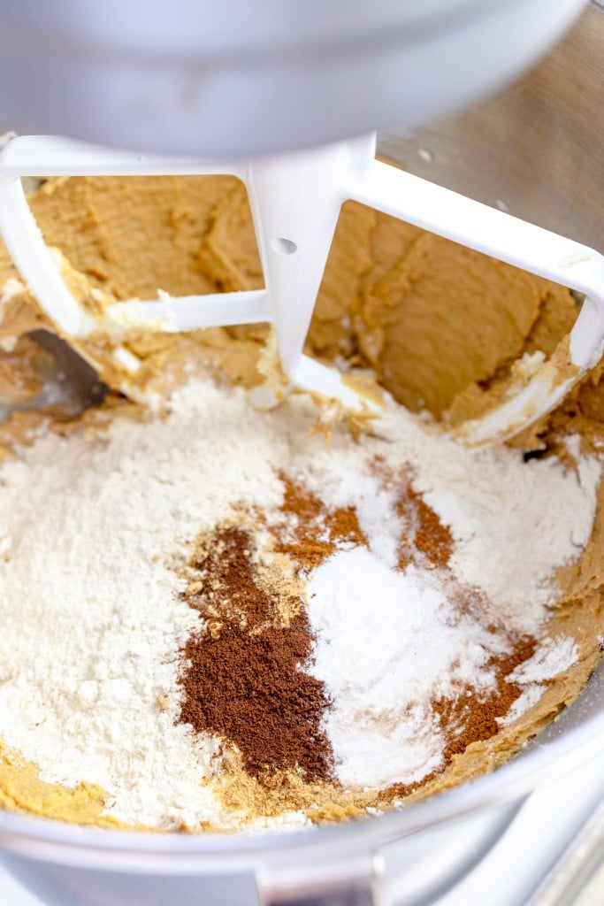 Close up of the bowl of a stand mixer with a paddle attachment mixing a creamed mixture with a flour mixture.