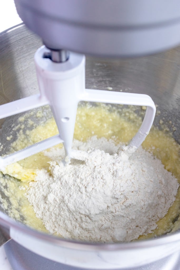 Close up of the bowl of a syand mixer with a paddle attachment mixing a creamed mixture with flour.