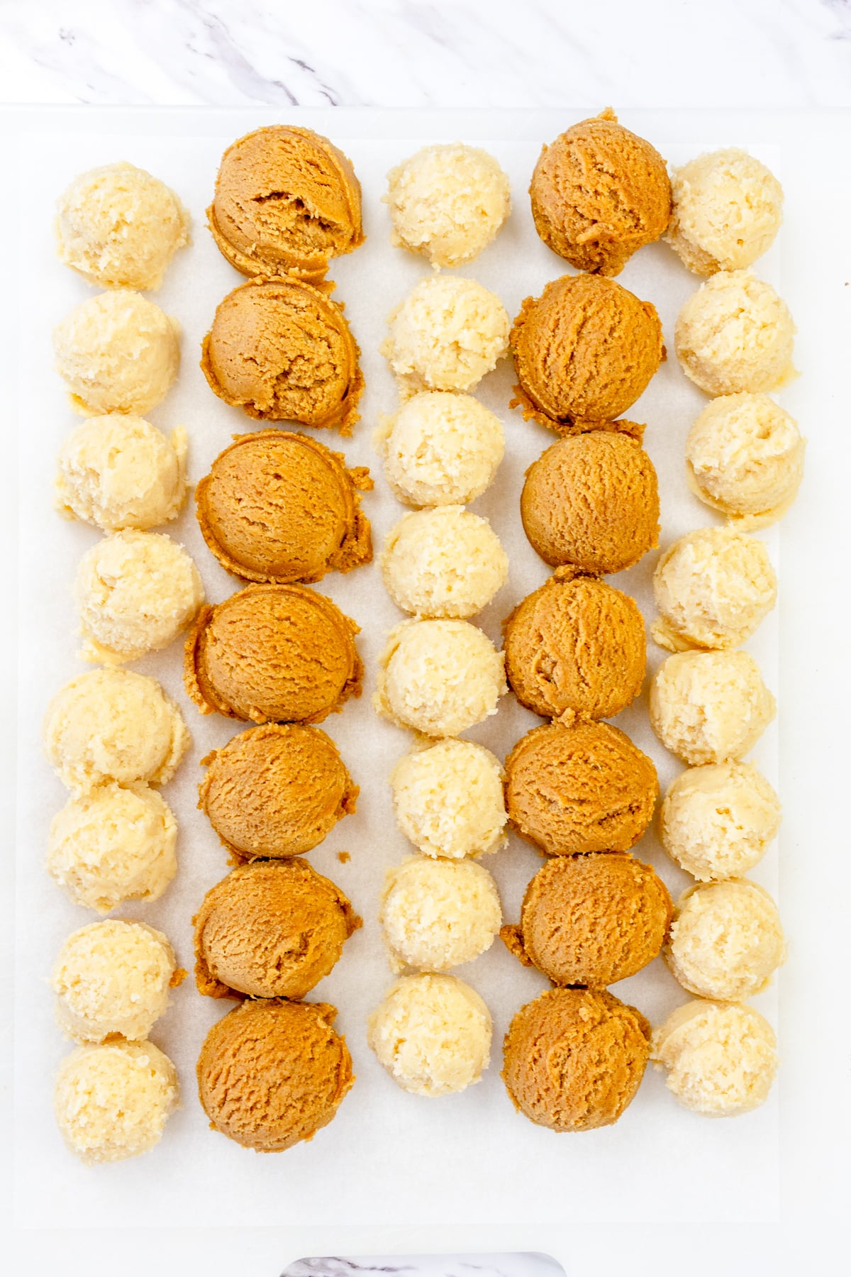 Top view of snickerdoodle cookie dough balls and gingersnap cookie dough balls lined up on a white surface.