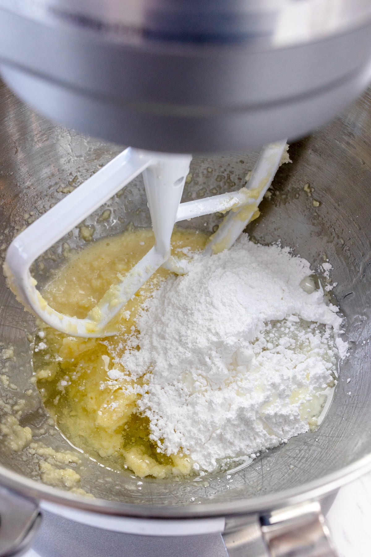 Close up of the bowl of a stand mixer with a creamed mixture and flour in it with a paddle attachment.