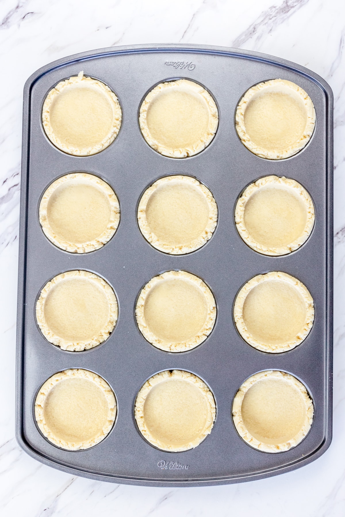 Top view of cobbler cookie bases in a muffin top baking tray.
