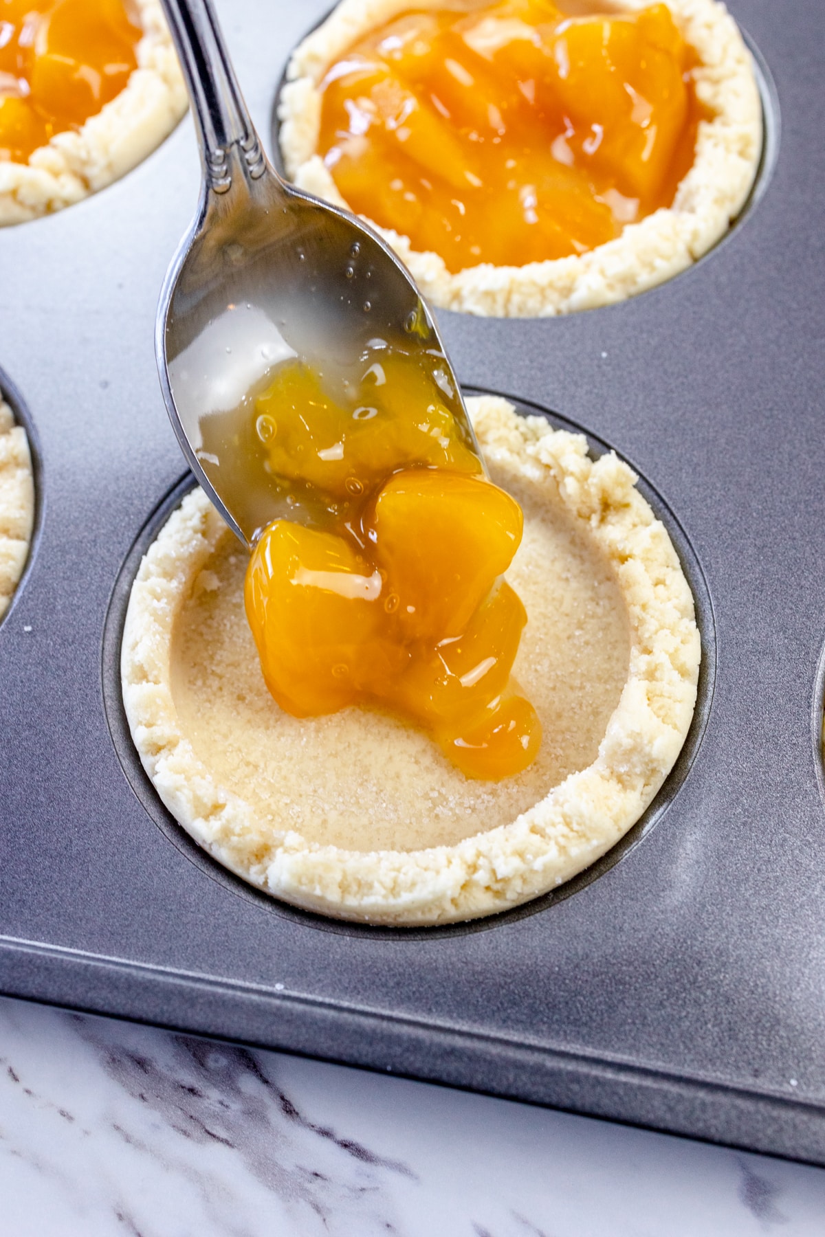 Close up of cobbler cookie bases being filled with peach pie filling.