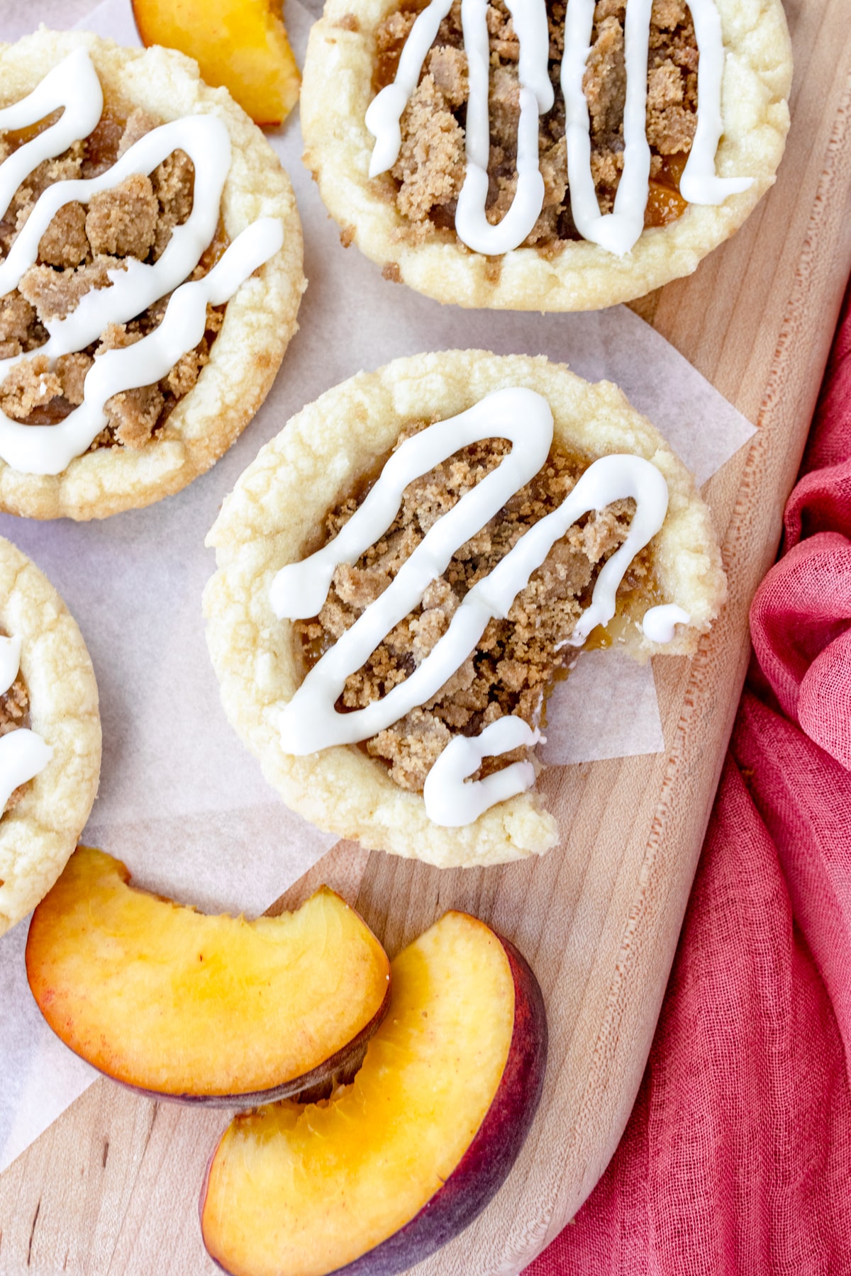Top view of peach cobbler cookies on a white surface with peach slices around them. 