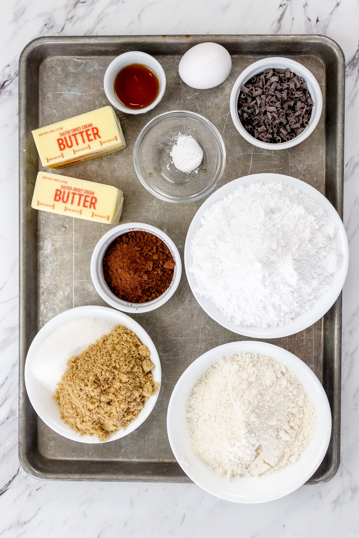 Top view of ingredients needed to make Chocolate Cake Cookies in small bowls on a baking tray.