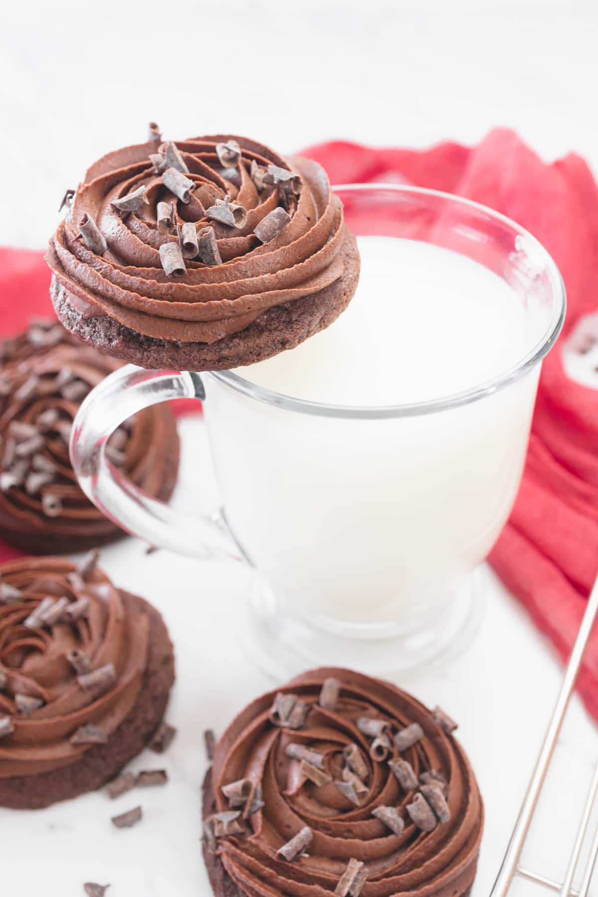 A glass of milk with a chocolate cake cookie resting on its brim.