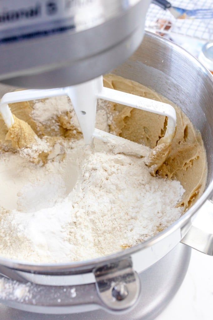 Close up of the bowl of a stand mixer with a creamed mixture topped with flour.
